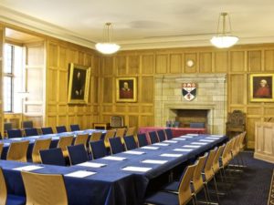 Inside parliament hall,  a wood panelled room with a long conference table and chairs. 